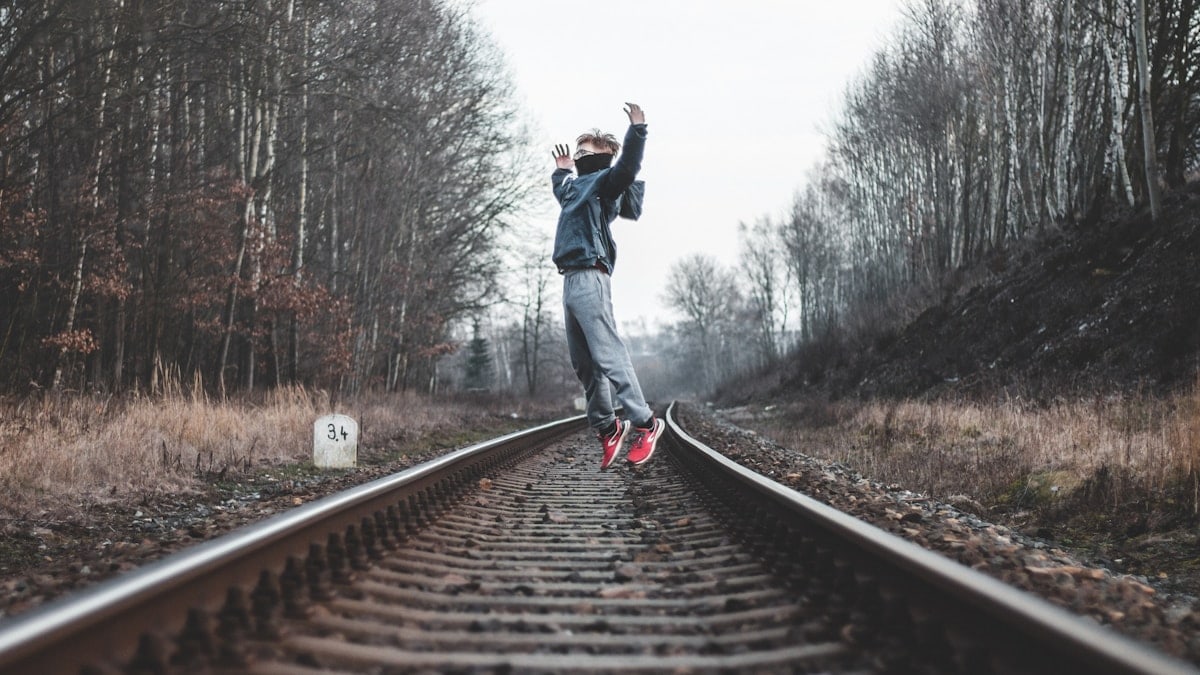 man in black jacket and blue denim jeans walking on train rail during daytime